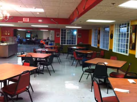 Bright dining area with red-accent chairs and multiple square tables in a communal space.