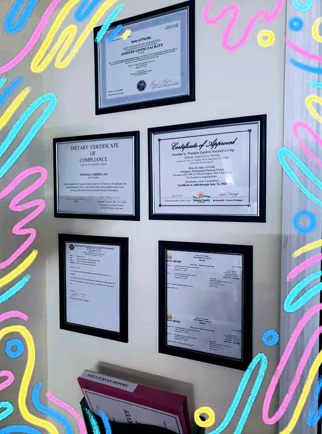 A wall displaying five framed certificates and documents related to Pinedale Gardens Assisted Living, including a dietary certificate of compliance and a certificate of approval. Below the frames, there is a shelf holding a binder labeled 'ANNUAL SURVEY REPORT'. The image is bordered with colorful abstract squiggles and shapes.