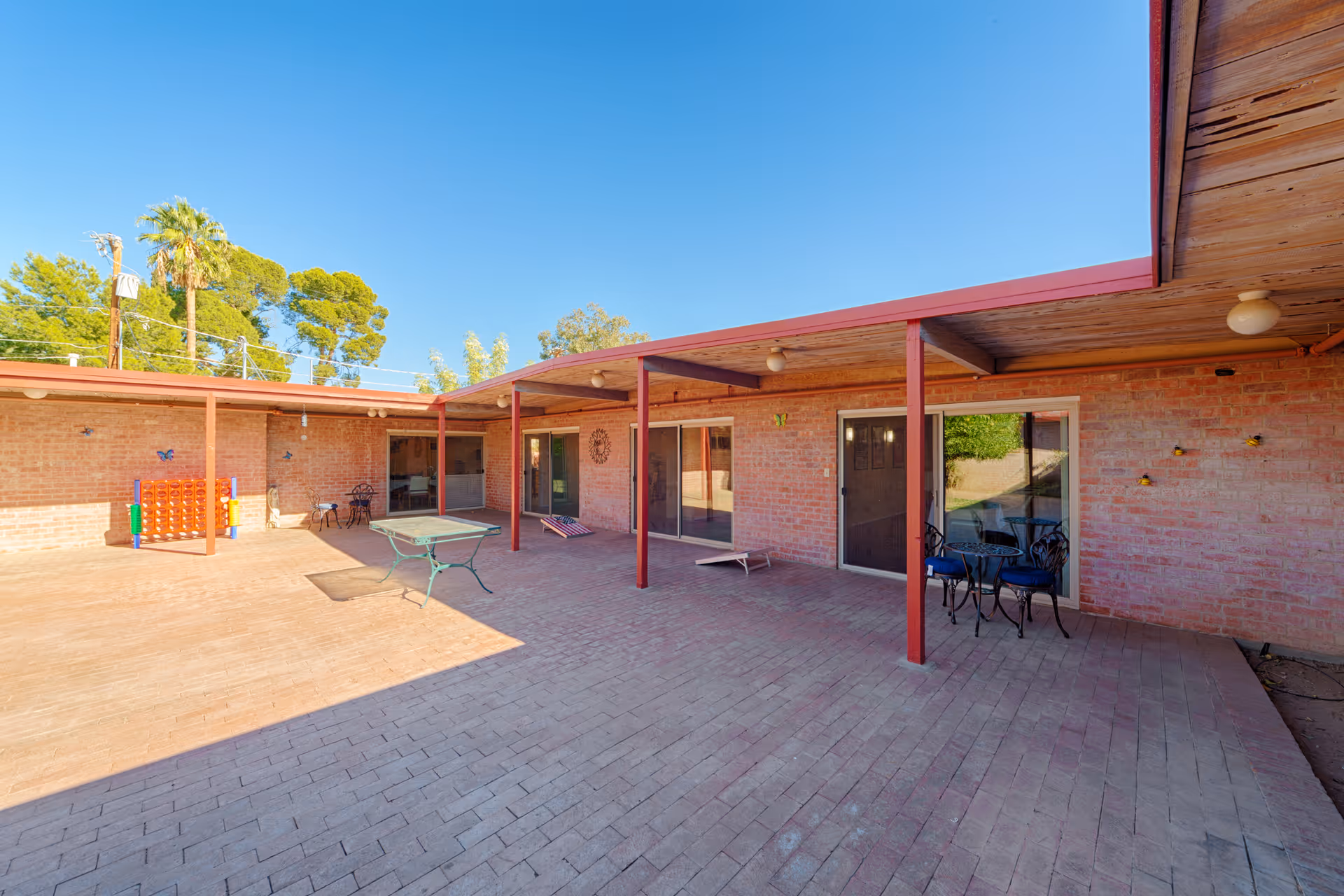 Brick courtyard with a covered patio, tables and chairs, and sliding glass doors at a senior living facility.