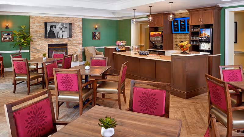 Dining room with wooden tables and magenta-upholstered chairs, a service counter/cafe area and a fireplace.