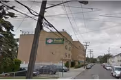 Street view of a multi-story brick building with a green sign that reads Bezalel Rehabilitation And Nursing Center. The building is located on a city street with parked cars along the curb and utility poles with overhead wires.