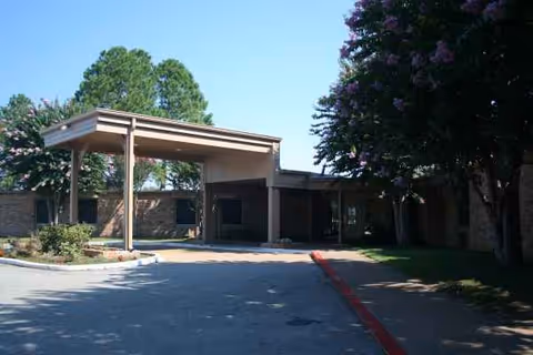 The nursing facility's brick exterior with a covered entry driveway and surrounding trees.