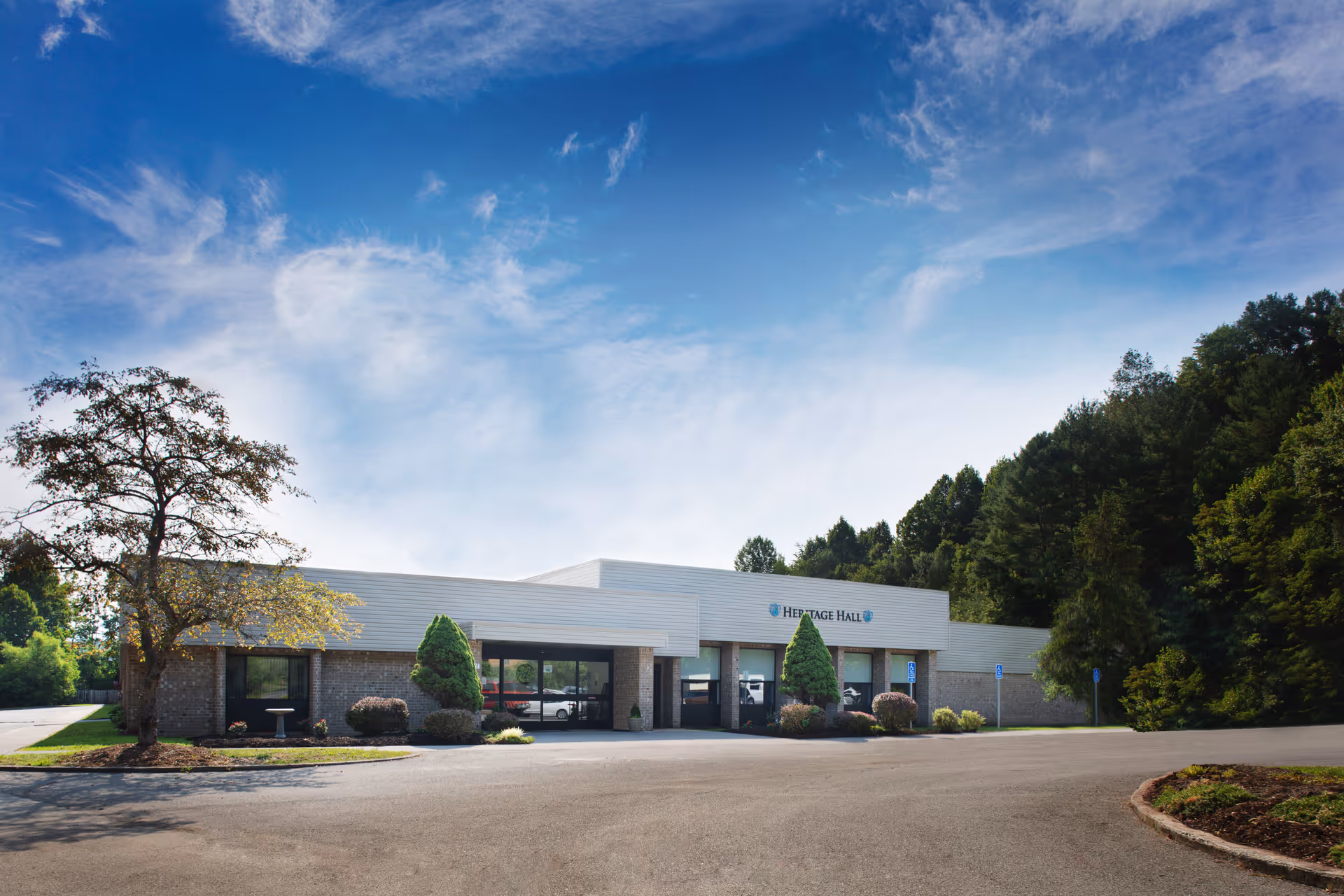 Exterior view of Heritage Hall Big Stone Gap building with a clear blue sky, surrounded by trees and a parking area in front.