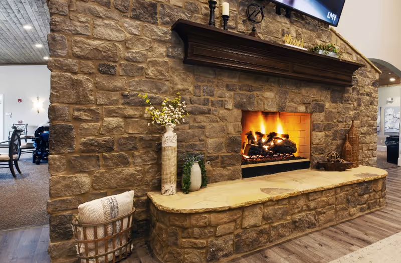 A stone fireplace with a burning fire in a lounge area decorated with vases, a basket, and seating visible nearby.