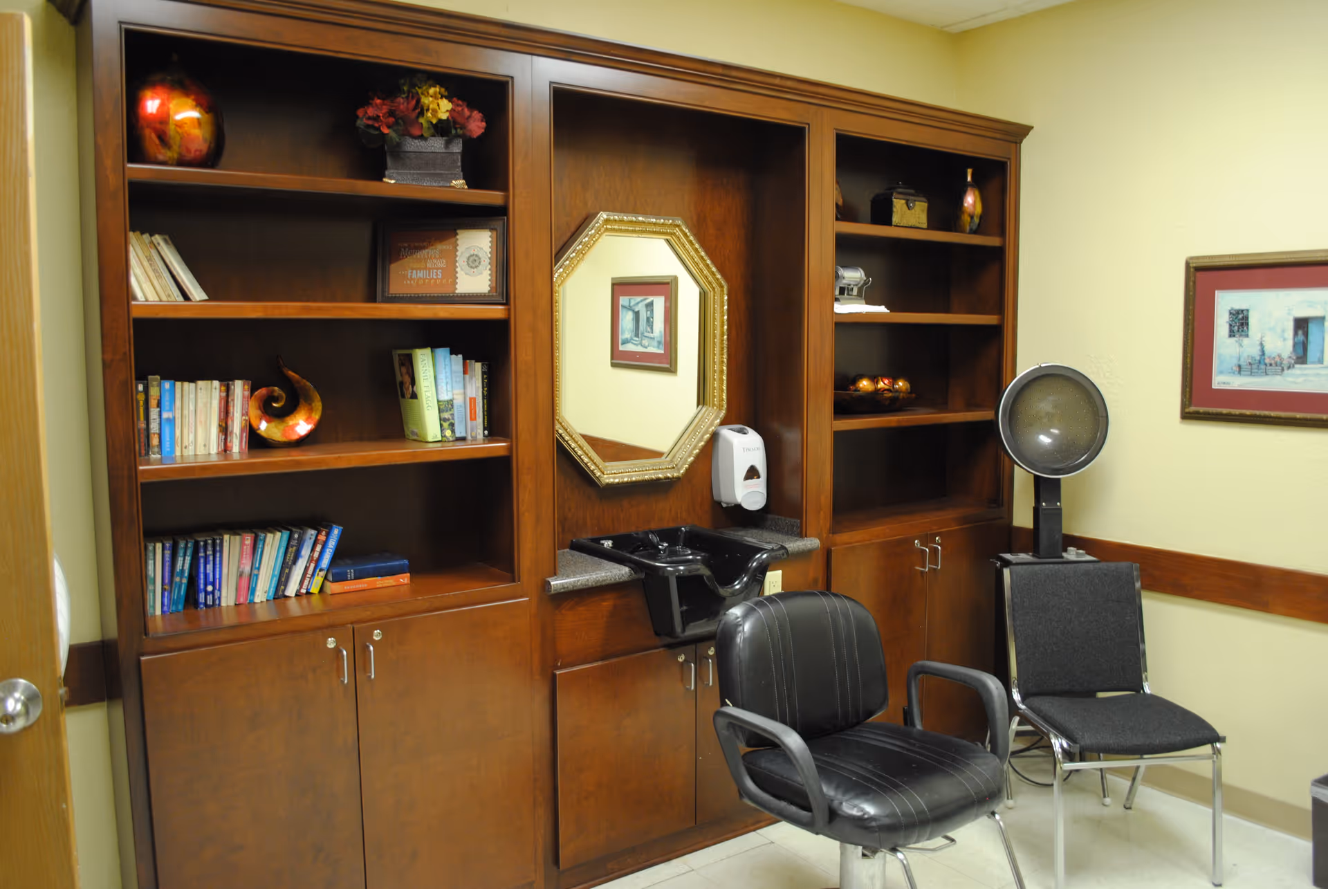 Interior room with wooden built-in shelves, a mirror and sink, a salon chair and a hooded hair dryer.