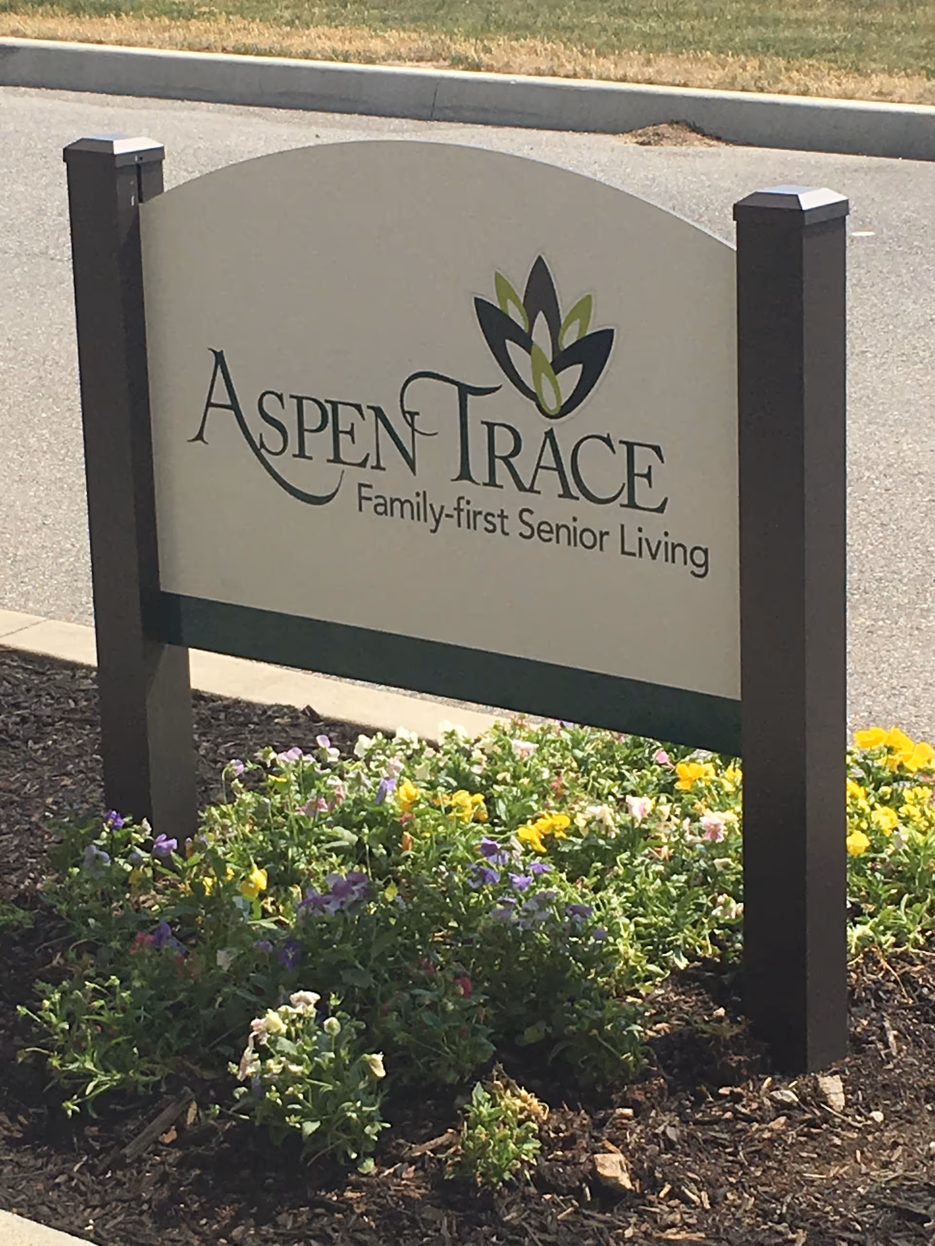 A landscaped entrance sign that reads "Aspen Trace Family-first Senior Living" surrounded by flowers.