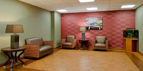 A cozy, furnished lounge with two armchairs, a sofa, lamps, wall art, and an aquarium.