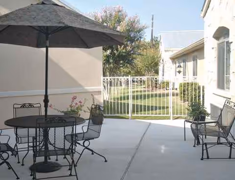 Outdoor patio with metal tables, chairs, and a large umbrella beside a light building.