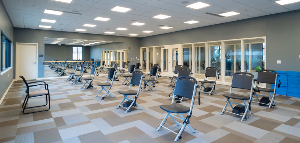 Spacious fitness/studio room with rows of folding exercise chairs, a mirrored wall, and ballet barres.