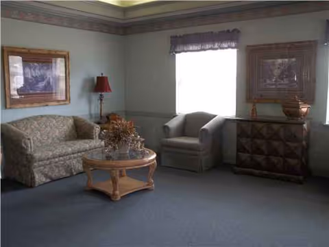 Sitting area with sofa, armchair, coffee table, lamp, and artwork in a furnished living room.