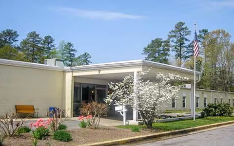 Front exterior view of Chesapeake Shores Nursing Center with entrance canopy, flagpole, and blooming trees.