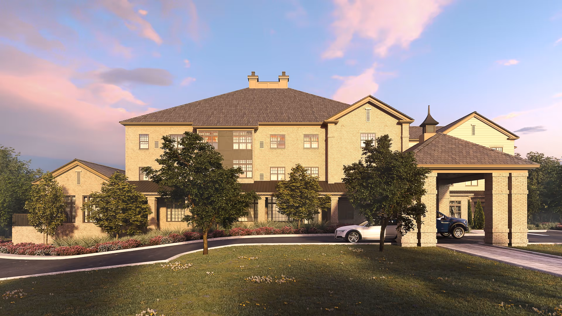 Exterior view of a large, multi-story senior living facility building with beige brick walls and a gray shingled roof under a partly cloudy sky at sunset. The building has multiple windows and a covered entrance with two cars parked underneath. There are several trees and landscaped bushes in front of the building along a curved driveway.