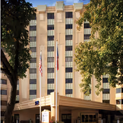 Front exterior of a multi-story residential building with flagpoles and trees at the entrance.