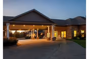 Exterior view of a nursing and rehab facility at dusk with a covered entrance, lit windows, and a curved driveway.