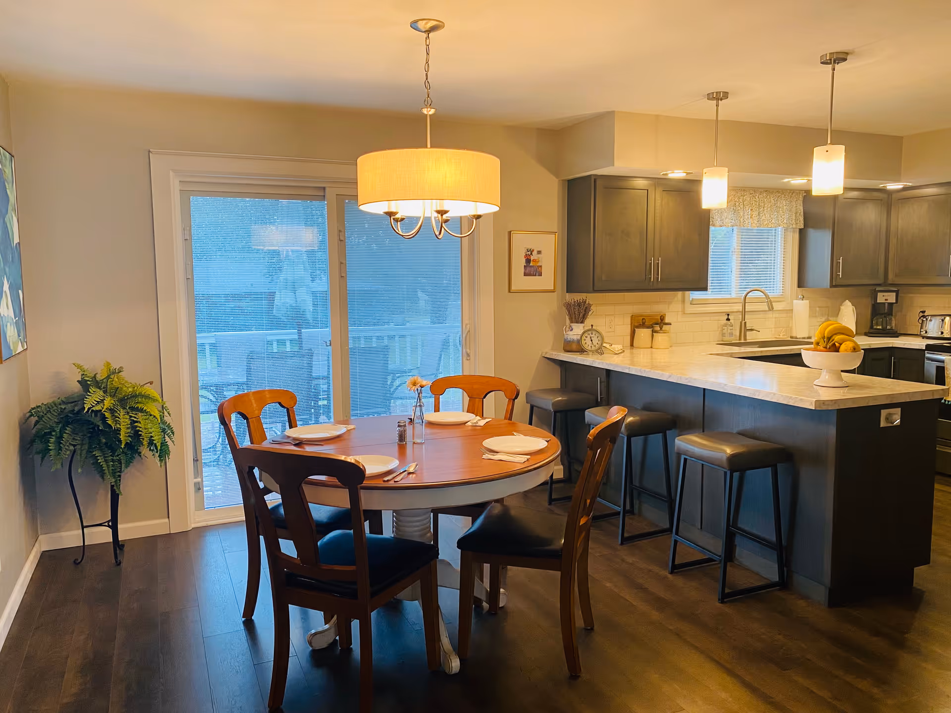 Bright open dining area with a round wooden table set for four next to a modern kitchen island with bar stools.