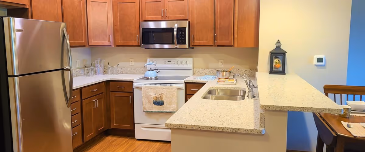 Modern kitchen with stainless-steel refrigerator, white stove and microwave, wooden cabinets, and a breakfast bar with a sink.
