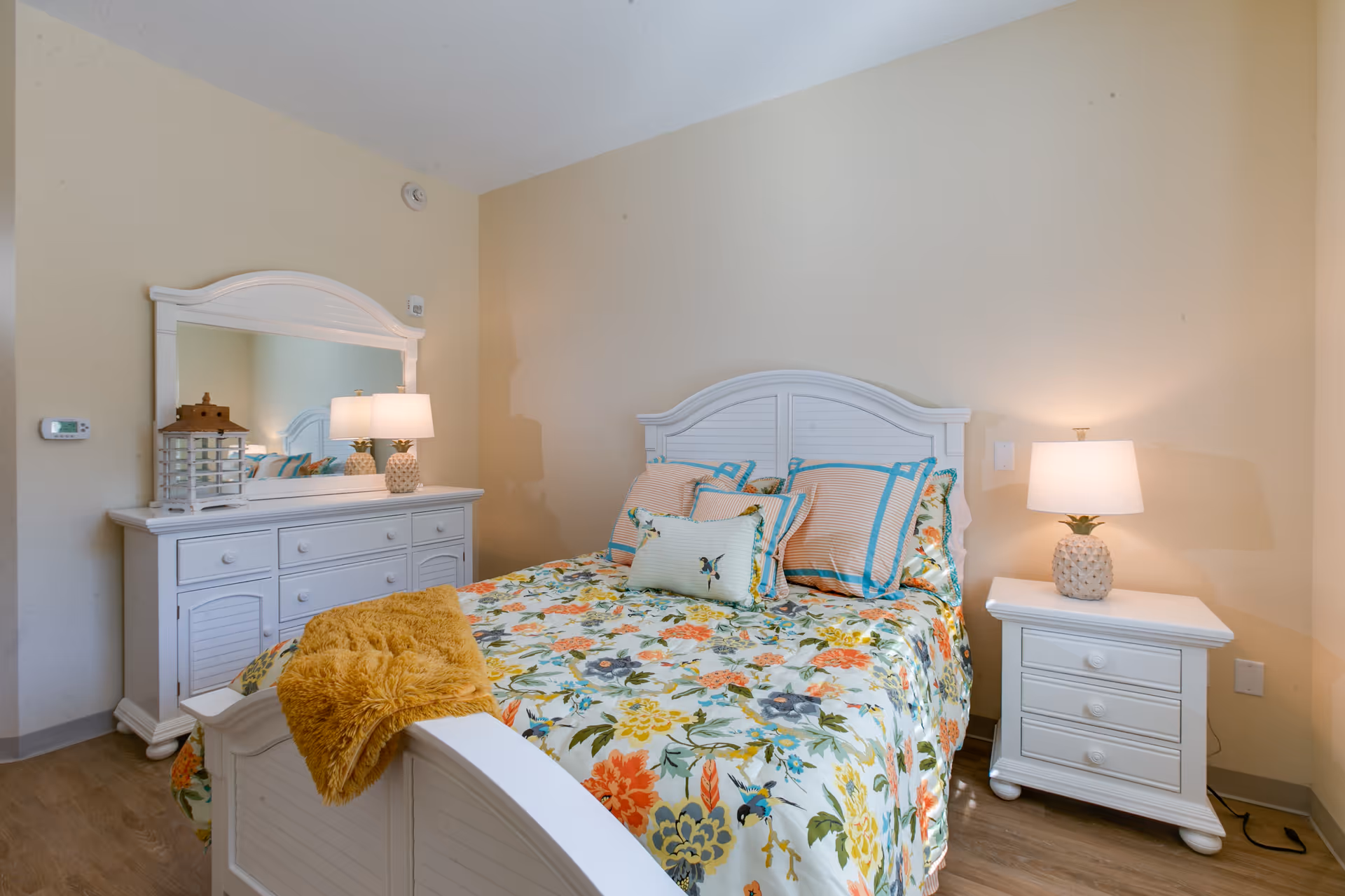 White bedroom with floral bedding, matching dresser, nightstands, and lamps.