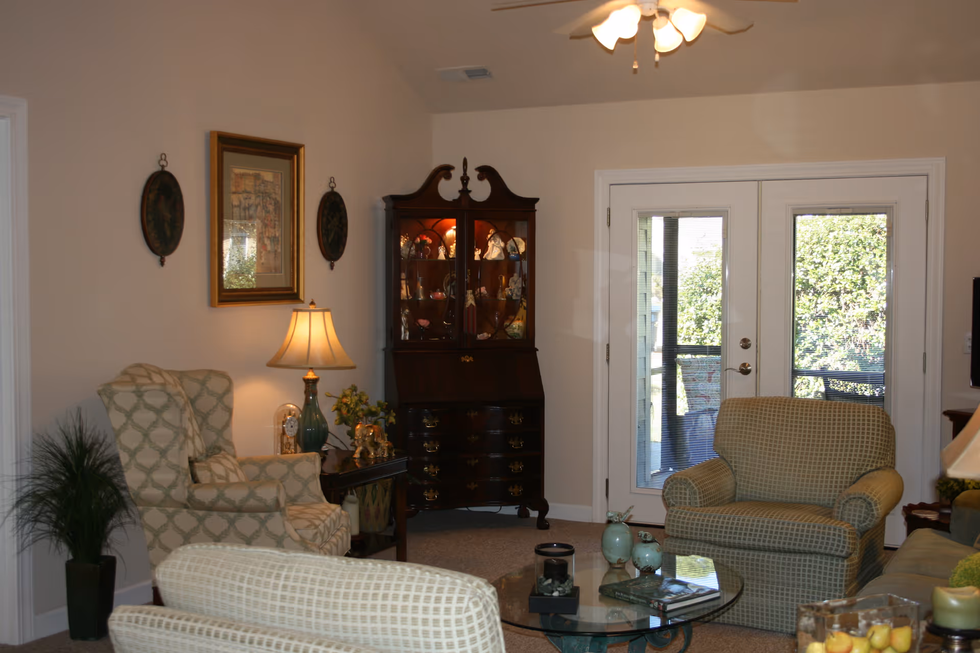 Living room with upholstered armchairs, a glass coffee table, a display cabinet and French doors to the outside.