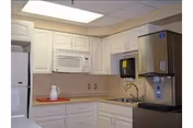 Compact kitchenette with white cabinets, a microwave above the counter, a sink, refrigerator, and a water dispenser.