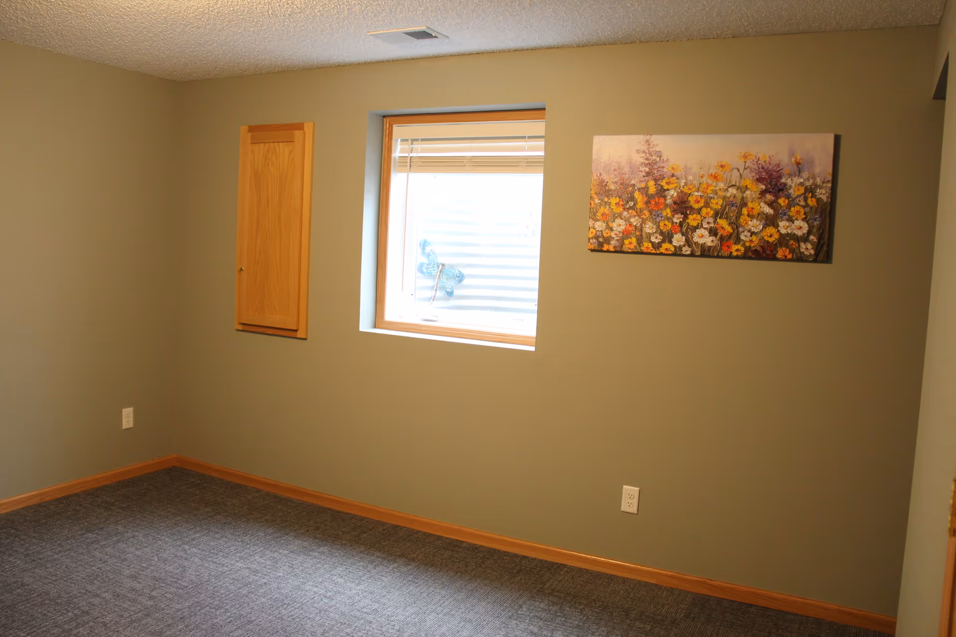 Small empty room with a window, floral wall art, carpeted floor and pale green walls.