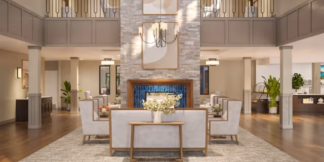 Elegant senior living lobby with a central fireplace, neutral seating, plants, and chandelier.