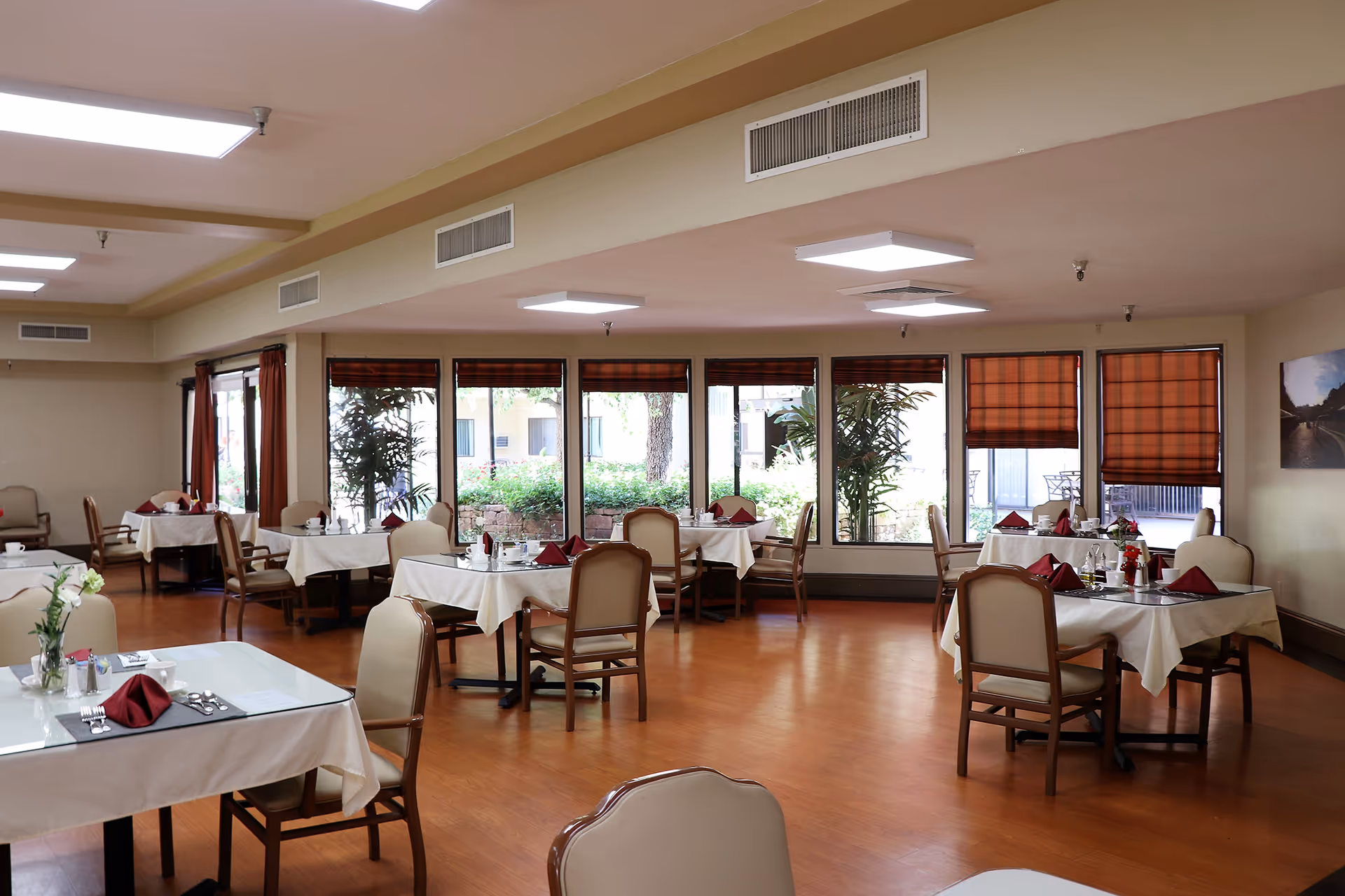 Spacious dining room with neatly set tables and chairs, large windows and hardwood floor.