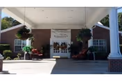 Front entrance of Williamsburg Nursing Home with hanging planters, chairs, and a covered walkway.