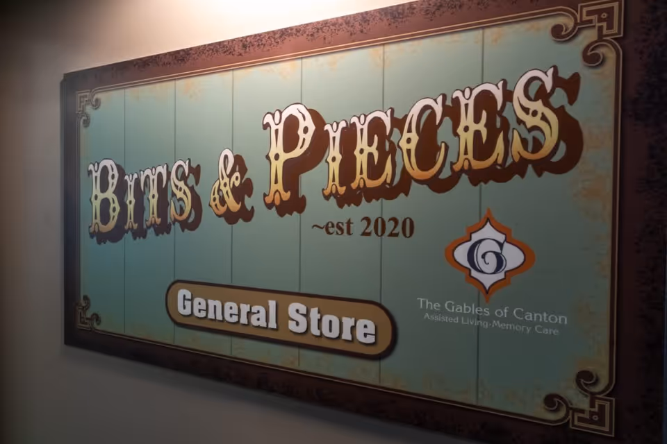 A vintage-style sign on a wall that reads 'Bits & Pieces ~est 2020 General Store' with a logo and text indicating it is part of The Gables of Canton, an assisted living and memory care facility.