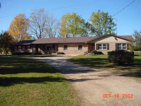 Single-story brick senior living facility exterior with a driveway and grassy lawn.