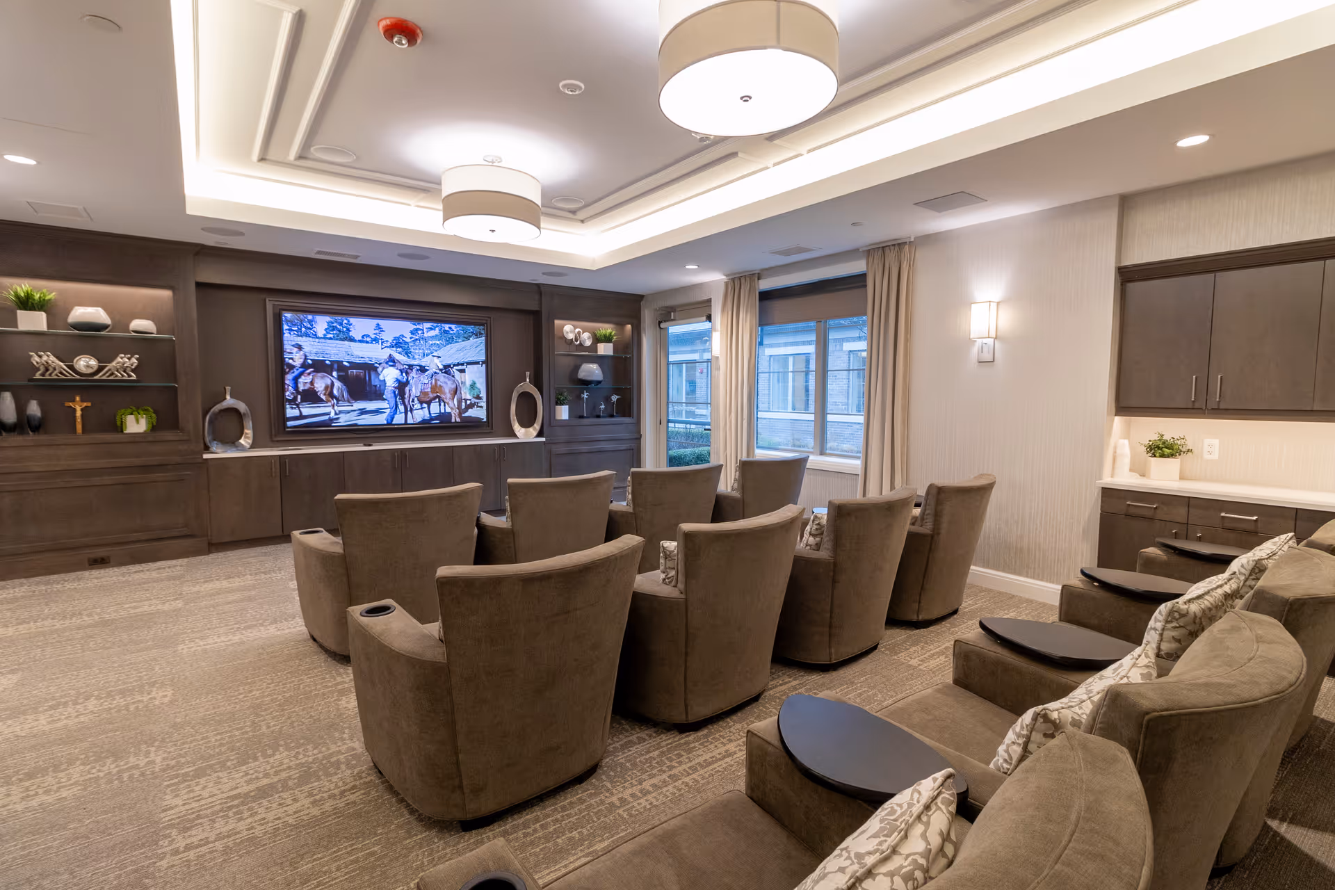 Media room with upholstered recliner chairs arranged in rows facing a large wall-mounted TV and built-in cabinetry.