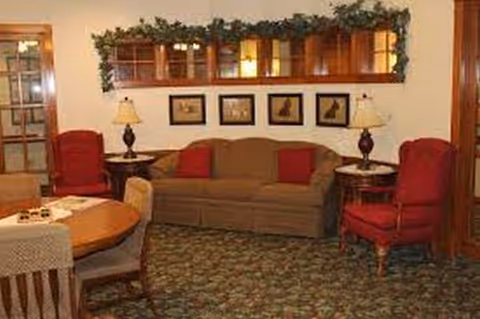 Cozy common living room with sofa, red chairs, lamps, framed pictures, green garland, and carpet.