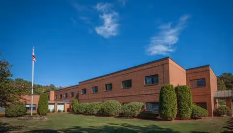 Brick senior living facility with manicured shrubs and a flagpole at the front.