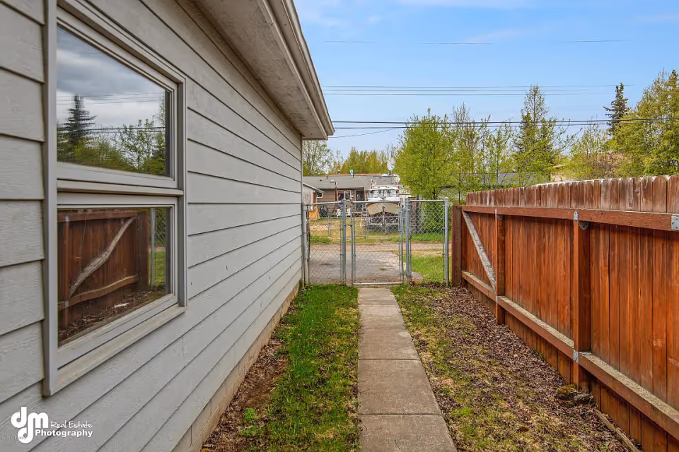 Narrow side yard with a concrete walkway between a house and a wooden fence leading to a chain-link gate.