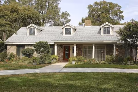 Front exterior of a single-story senior living building with a manicured lawn and trees.