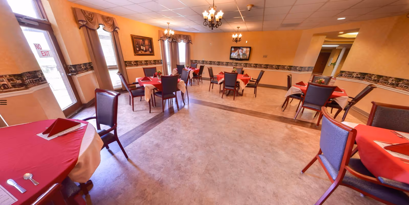 Dining room with multiple round tables covered in red tablecloths and chairs under chandeliers.
