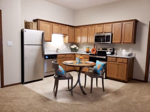 Open kitchen with oak cabinets, stainless steel appliances and a small round table with two chairs set in front.