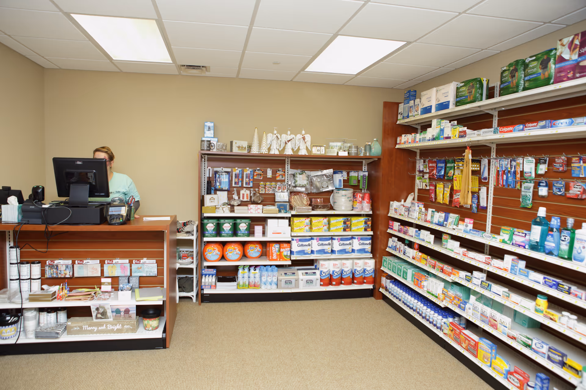 Interior of a small on-site shop at a retirement community with shelves of toiletries and supplies and a checkout counter with a staff member.