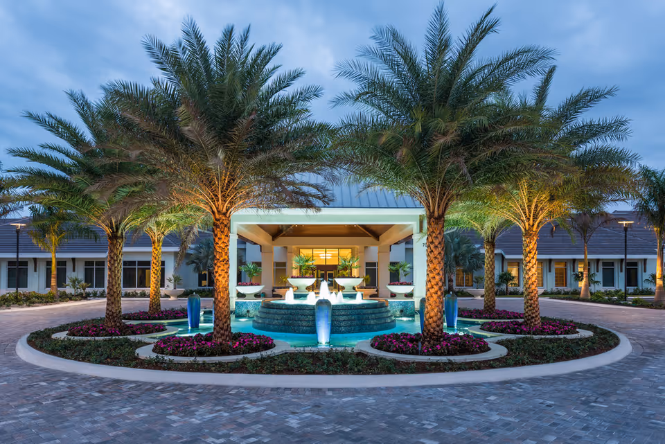 Exterior view of Vi at Bentley Village entrance with a fountain, palms, and landscaping.