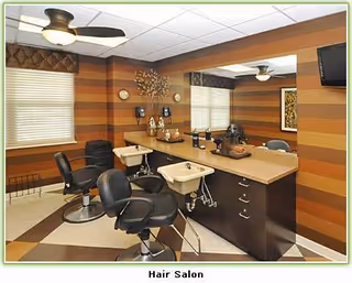 Interior view of a hair salon with two black salon chairs in front of two sinks and a large mirror. The walls have horizontal brown and tan stripes, and there are ceiling fans and window blinds.