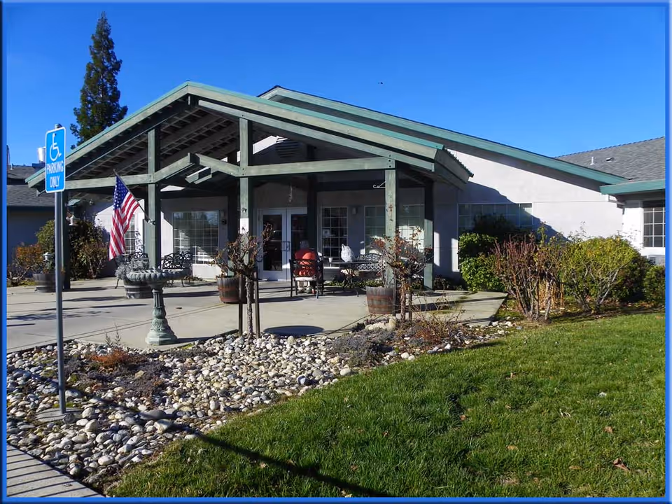 Front entrance of Amador Residential Care with a covered porch, outdoor seating, American flag, and landscaped rock beds.