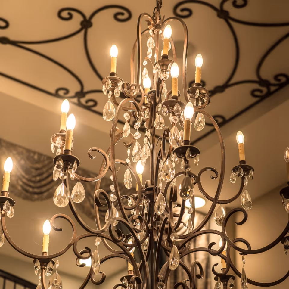 Ornate crystal chandelier with multiple lit candle-style bulbs hanging from a decorative ceiling.