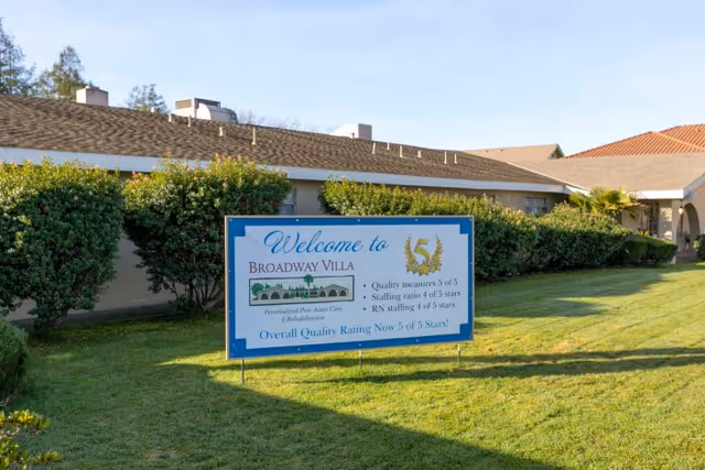 A 'Welcome to Broadway Villa' sign on a grassy lawn in front of a low, single-story building with hedges.