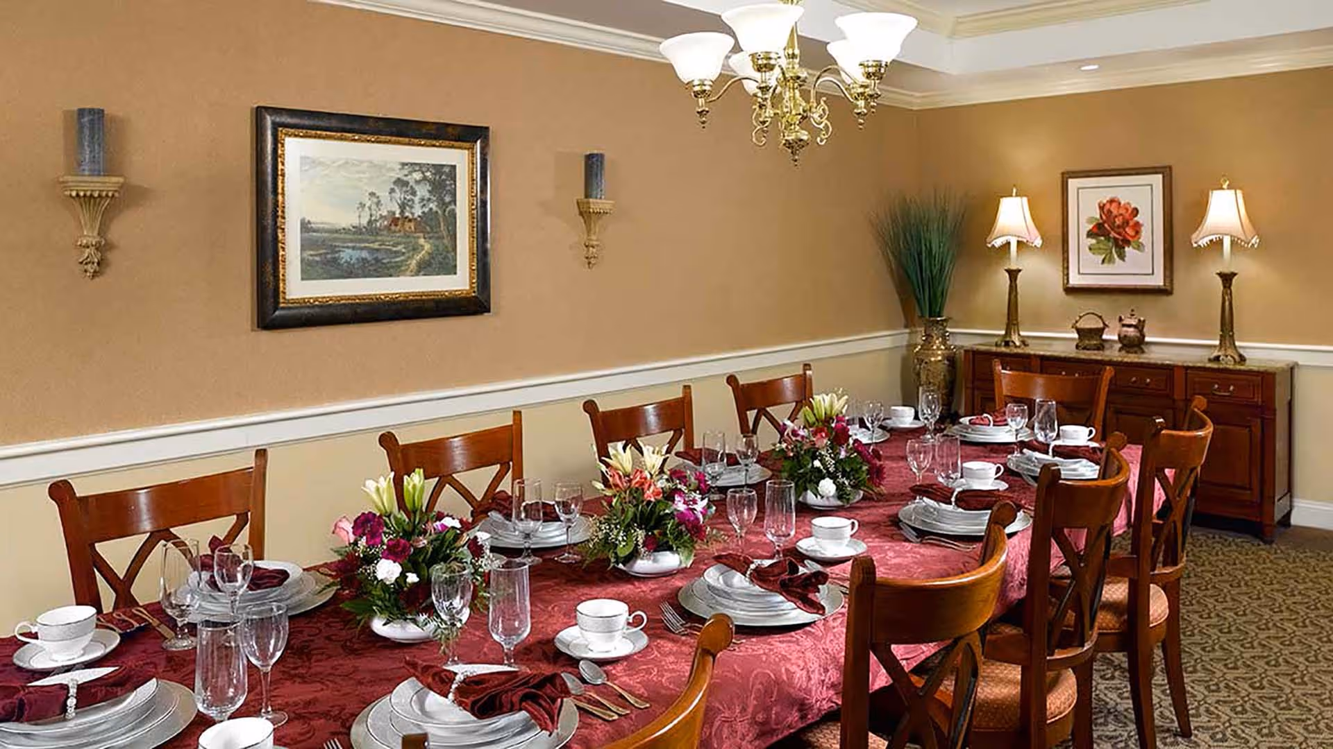 Formal dining room with a long table set with plates, glassware, napkins and floral centerpieces under a chandelier.