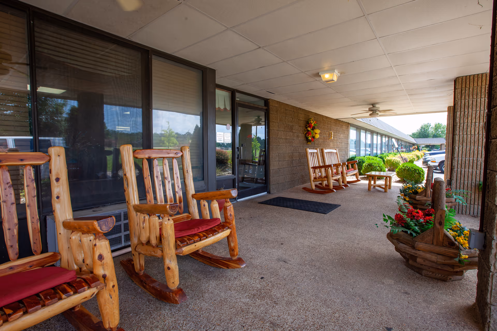 Covered front entrance walkway with wooden rocking chairs, decorative planters, and glass doors.