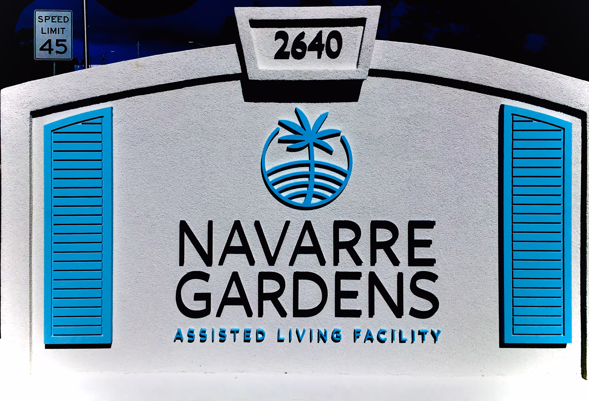 White entrance sign reading "NAVARRE GARDENS Assisted Living Facility" with the number 2640 and blue decorative accents.