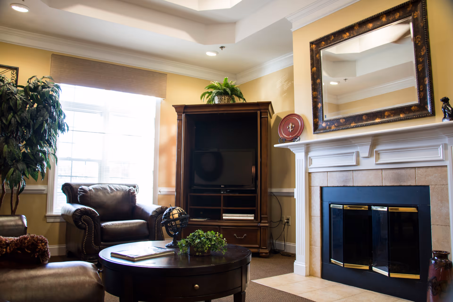 Cozy living room with leather armchairs, a round coffee table, TV cabinet, and a fireplace topped by a large mirror.