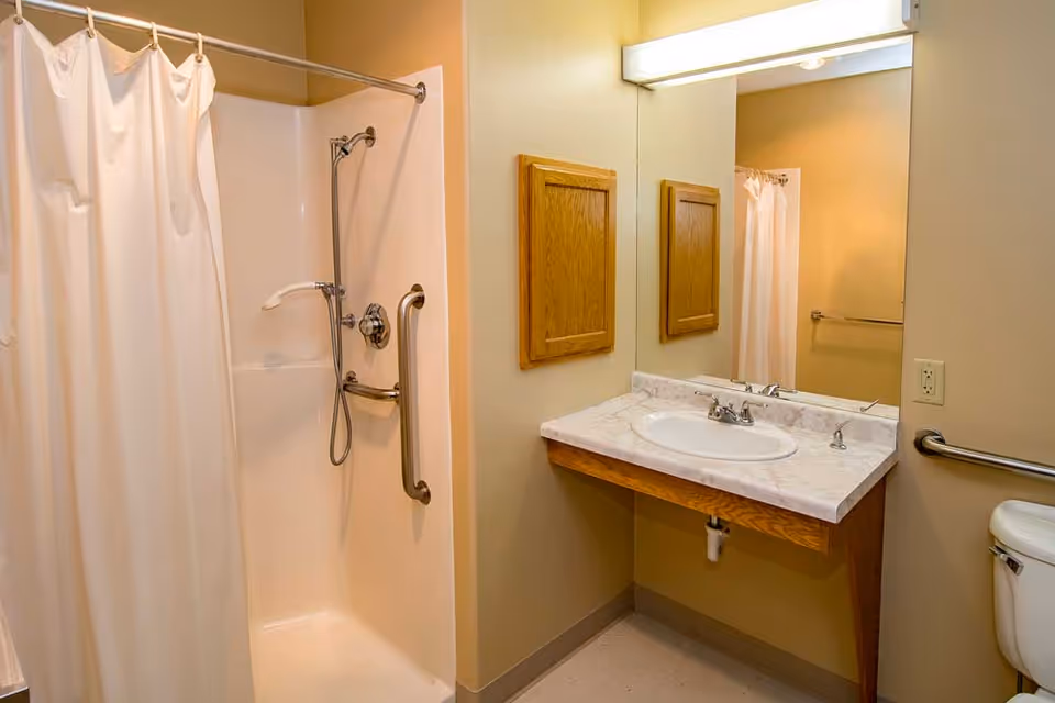 A clean bathroom featuring a shower with a curtain, a sink with a marble countertop, and a mirror on the wall.