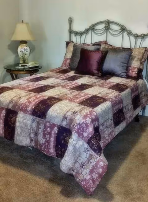 A neatly made bedroom featuring a decorative quilt, pillows, metal bed frame, and nightstand.
