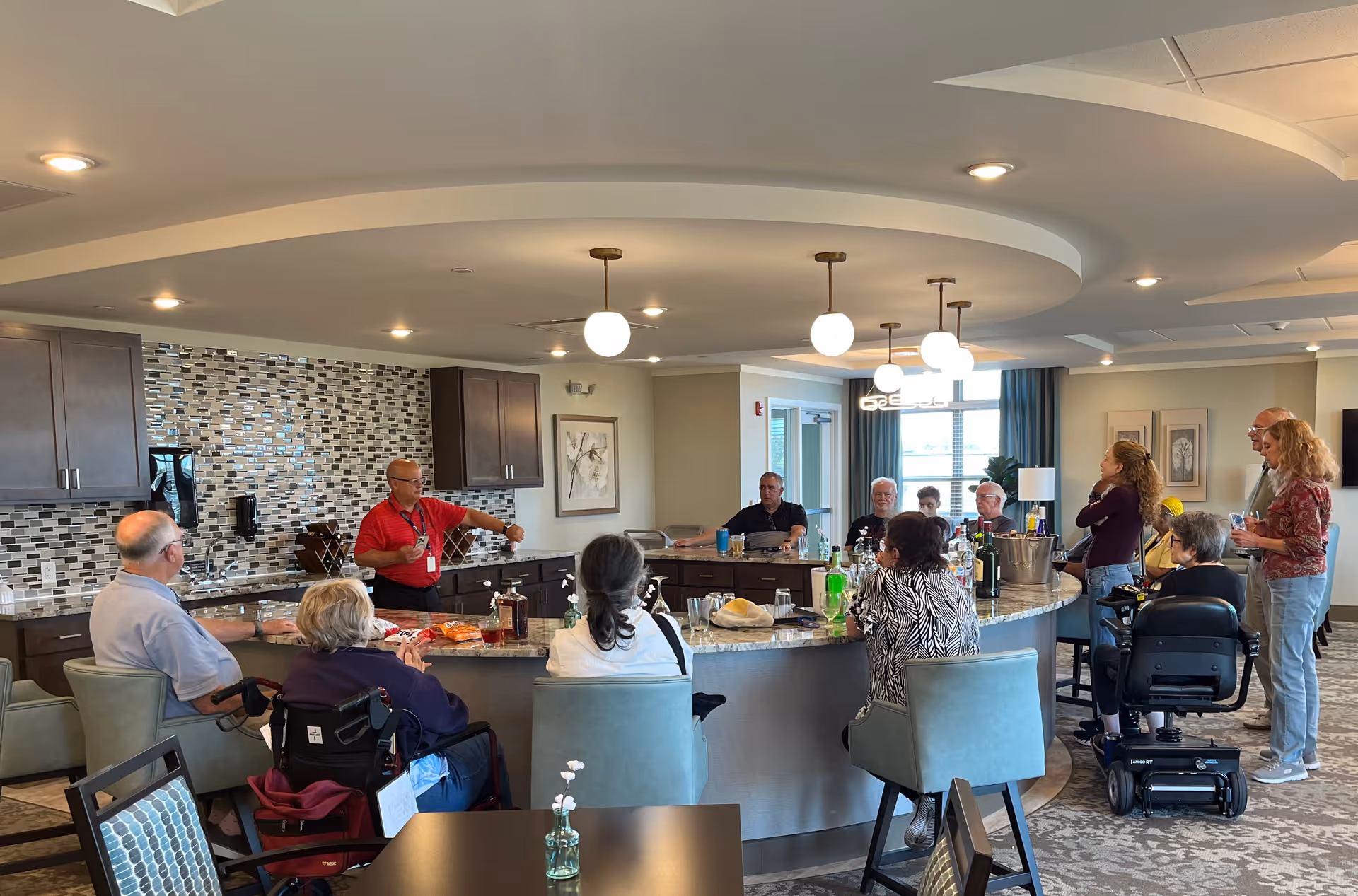 Residents and staff gathered around a large curved kitchen island in a communal dining/activity room.