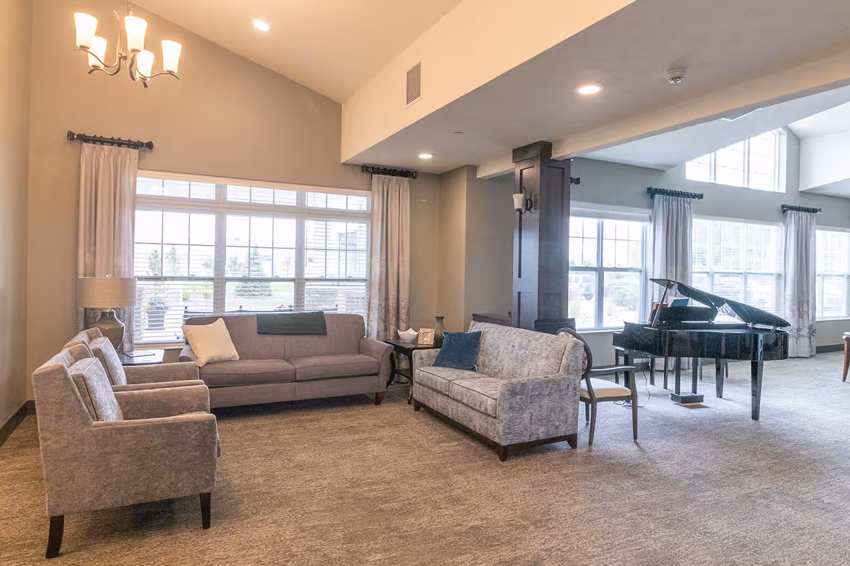 Spacious communal living room with sofas, armchairs, large windows, and a black grand piano.